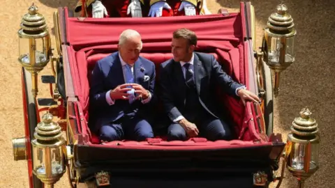 King Charles and Macron, both wearing suits, in a carriage