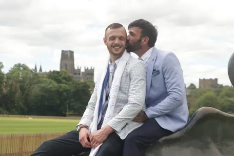 Newlyweds John, 39, and Les, 50, both in suits, sat atop Durham&#x27;s riverside bull sculpture.