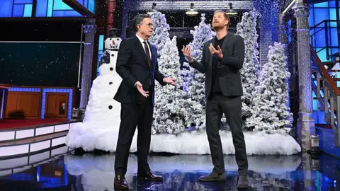 Stephen Colbert and Prince Harry on the set of the show with fake snow, Christmas trees and a snowman