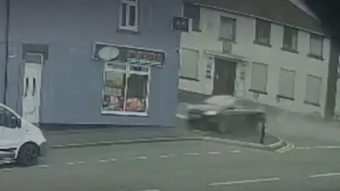 A car is seen damaged after it has hit a grey coloured building.