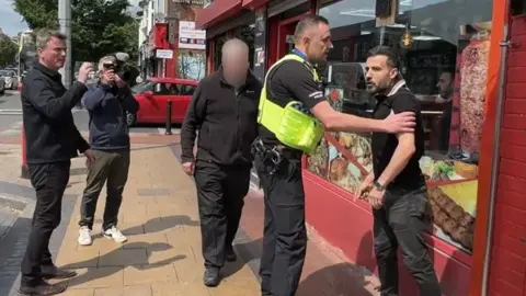 Ed Thomas and a cameraman film police holding back a shop owner